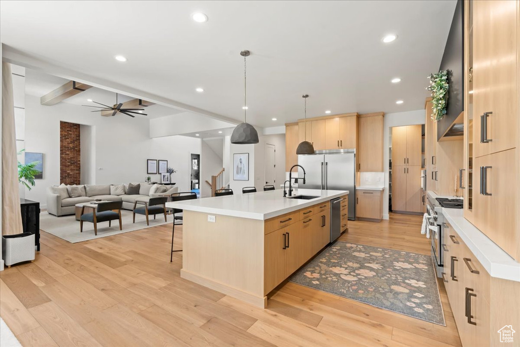 Kitchen featuring light brown cabinetry, high end appliances, a center island with sink, ceiling fan, and light wood-style floors