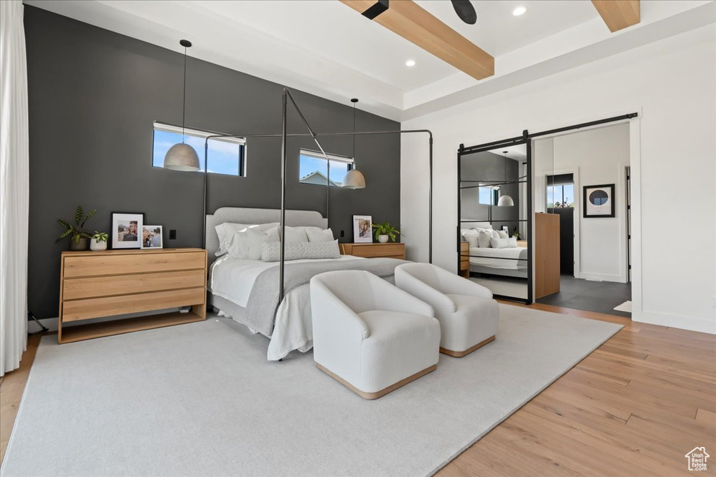Bedroom featuring light wood-style floors, beamed ceiling, multiple windows, a barn door, and recessed lighting