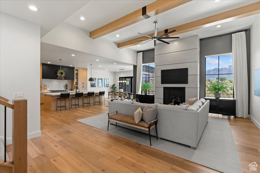 Living area with beamed ceiling, light wood-style flooring, recessed lighting, ceiling fan, and a large fireplace