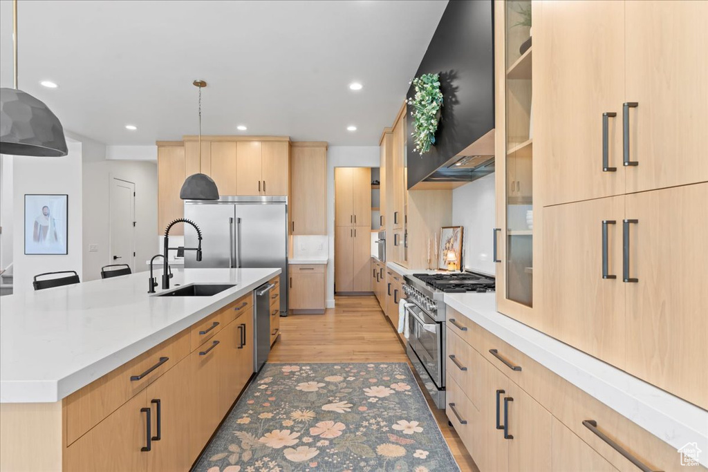Kitchen with light brown cabinets, high quality appliances, a sink, light wood finished floors, and recessed lighting