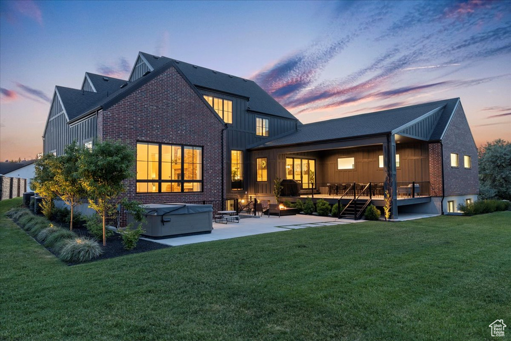 Back of house at dusk featuring brick siding, a patio, a hot tub, and board and batten siding