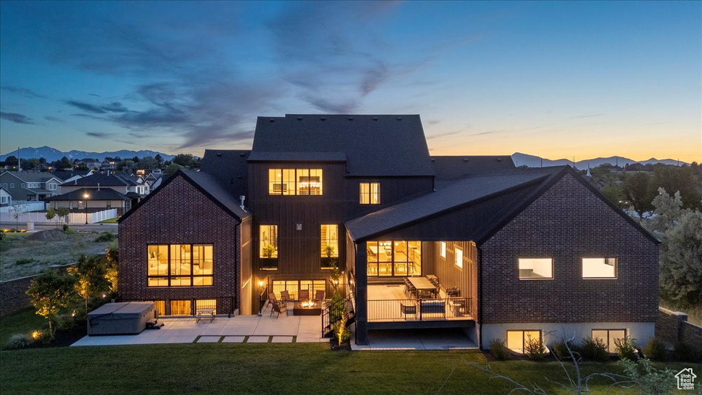 Back of property at dusk featuring a patio, a lawn, brick siding, and a mountain view