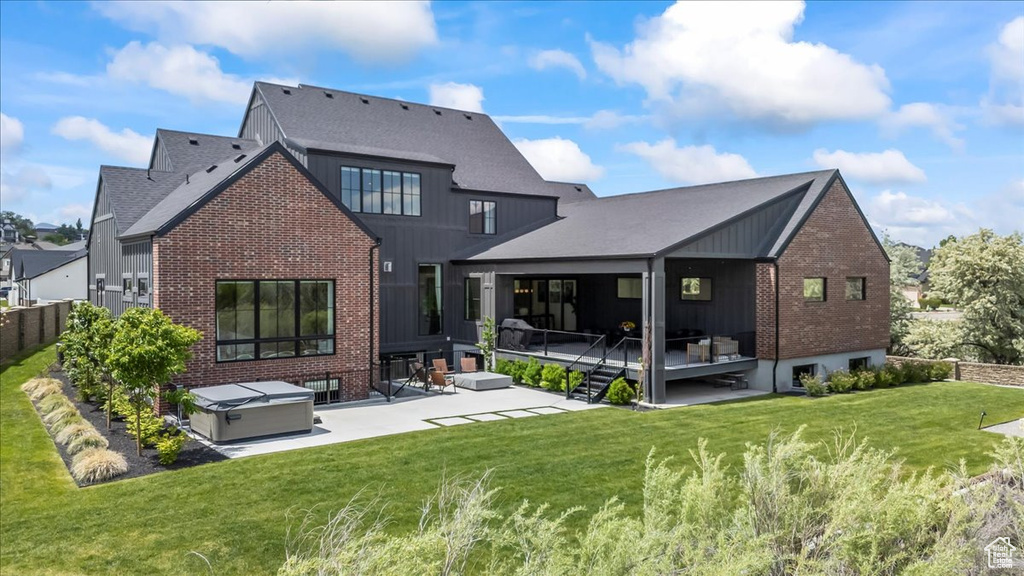 Rear view of property with brick siding, a patio area, a yard, and a hot tub