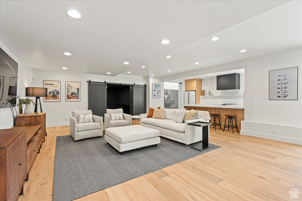Living area with a barn door, light wood finished floors, recessed lighting, and baseboards