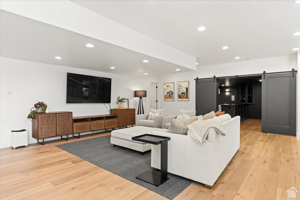 Living room with a barn door, light wood finished floors, and recessed lighting