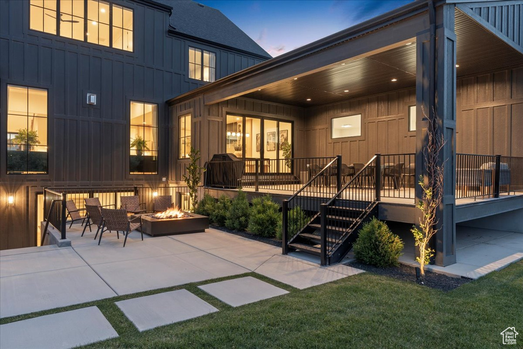 Back of house at dusk with board and batten siding, an outdoor fire pit, a patio area, and a lawn