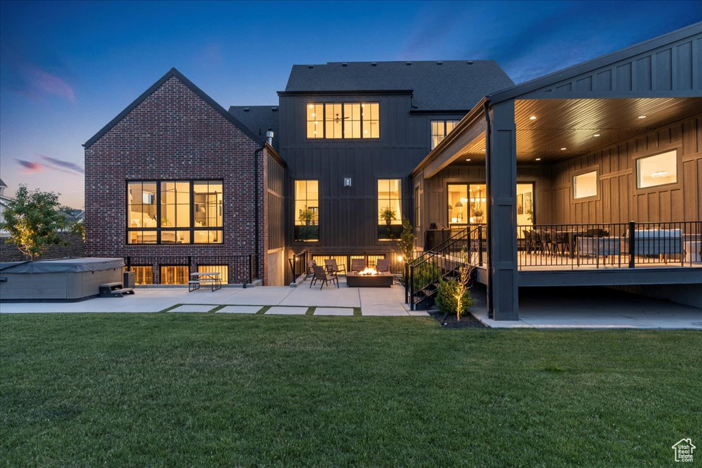 Rear view of house with a hot tub, a patio, a lawn, and brick siding