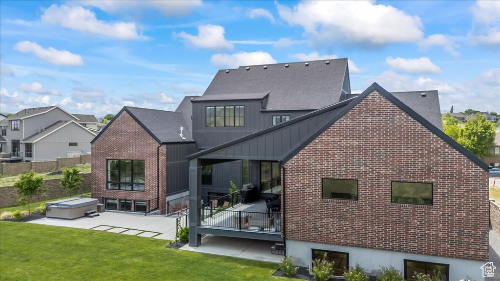 Back of property featuring a hot tub, a patio area, brick siding, and a residential view