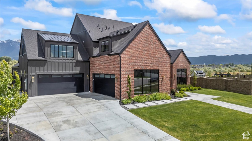 View of front of property with board and batten siding, an attached garage, driveway, brick siding, and a front lawn