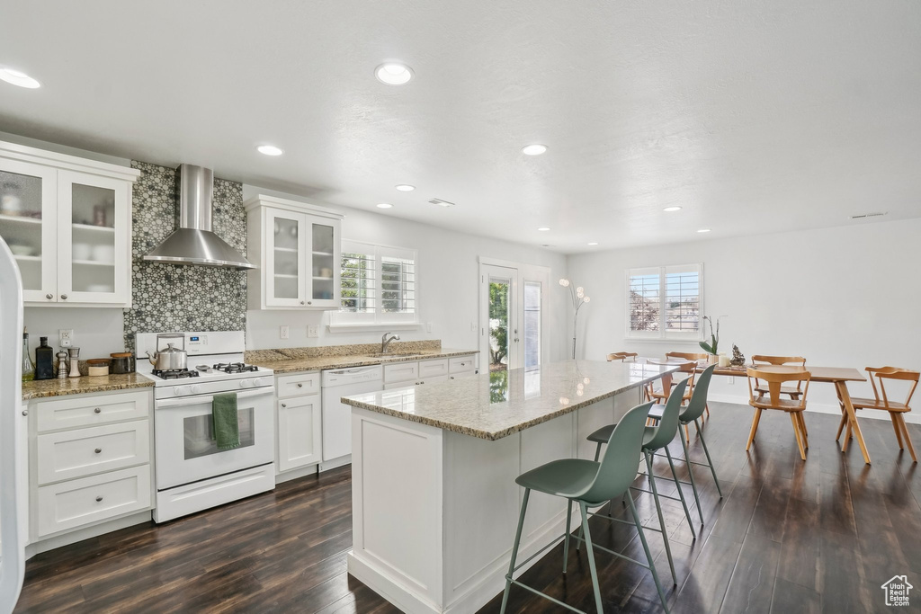 Kitchen with white appliances, wall chimney exhaust hood, a sink, healthy amount of natural light, and recessed lighting