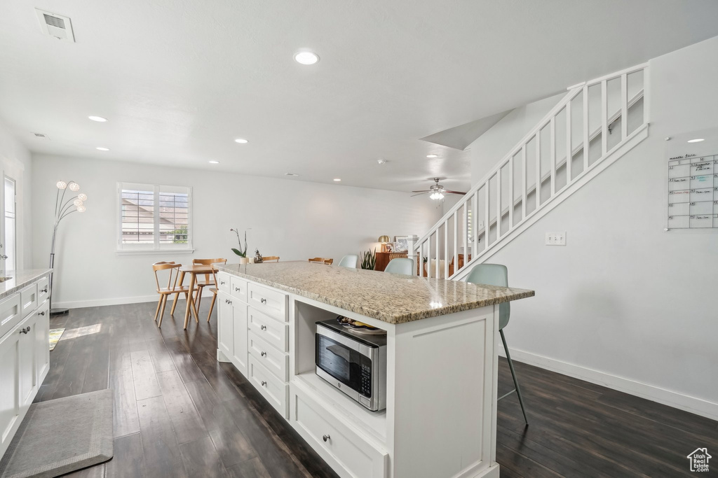 Kitchen featuring stainless steel microwave, a kitchen breakfast bar, baseboards, dark wood-style floors, and white cabinetry