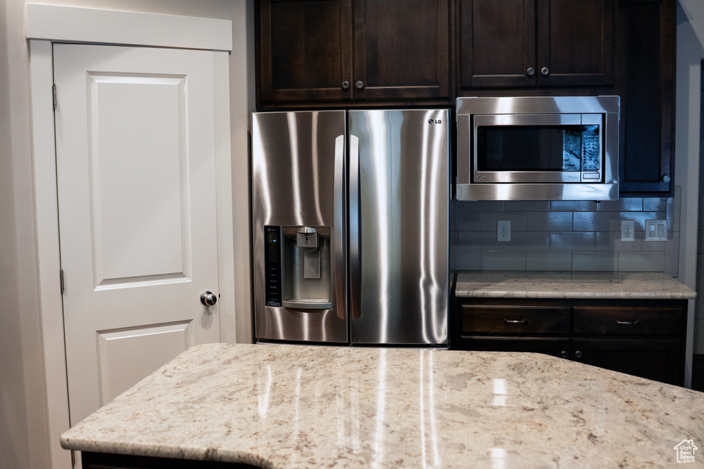 Kitchen with appliances with stainless steel finishes, backsplash, dark brown cabinetry, and light stone counters