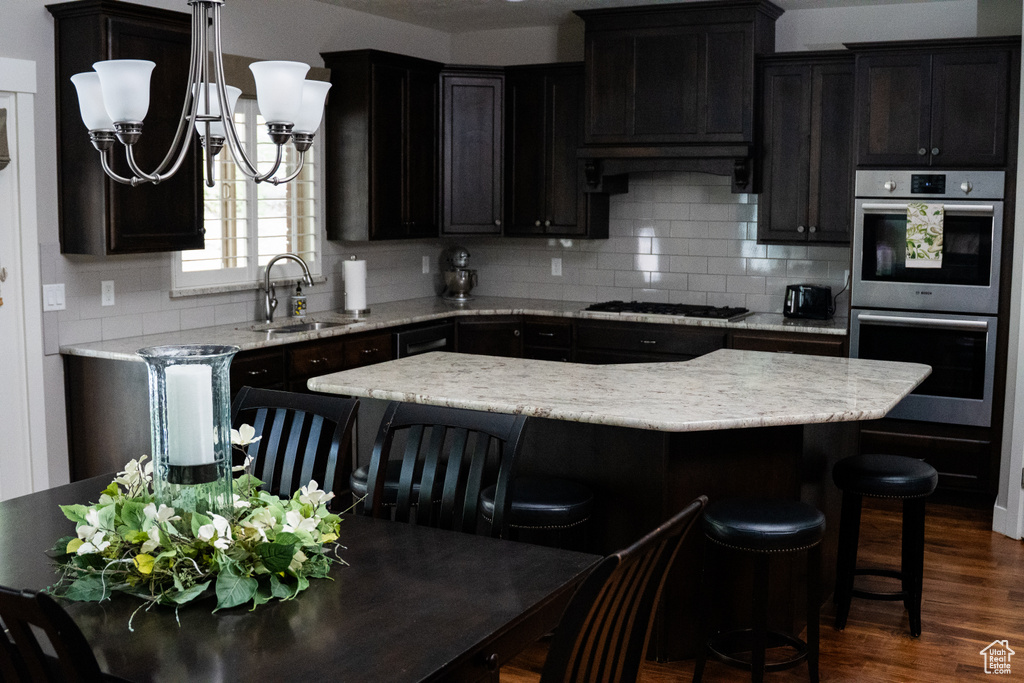 Kitchen with stainless steel double oven, a sink, black gas stovetop, tasteful backsplash, and a breakfast bar