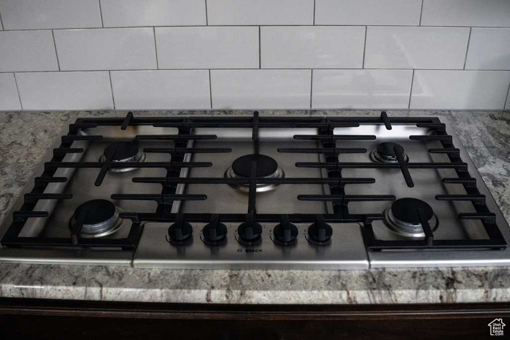 Kitchen view of stainless steel gas cooktop, tasteful backsplash, and light stone countertops
