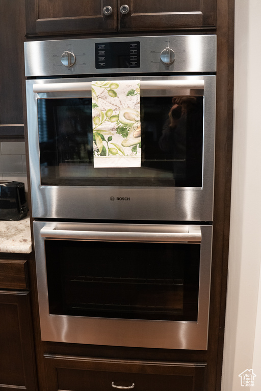 Kitchen view of dark brown cabinetry, double oven, light countertops, and tasteful backsplash
