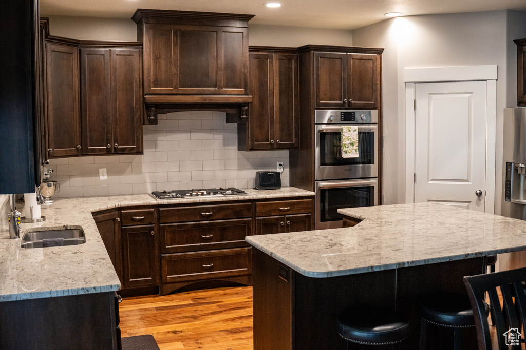Kitchen with appliances with stainless steel finishes, a sink, decorative backsplash, a kitchen bar, and dark brown cabinets