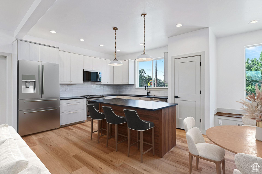Kitchen featuring appliances with stainless steel finishes, tasteful backsplash, a center island, white cabinetry, and a sink