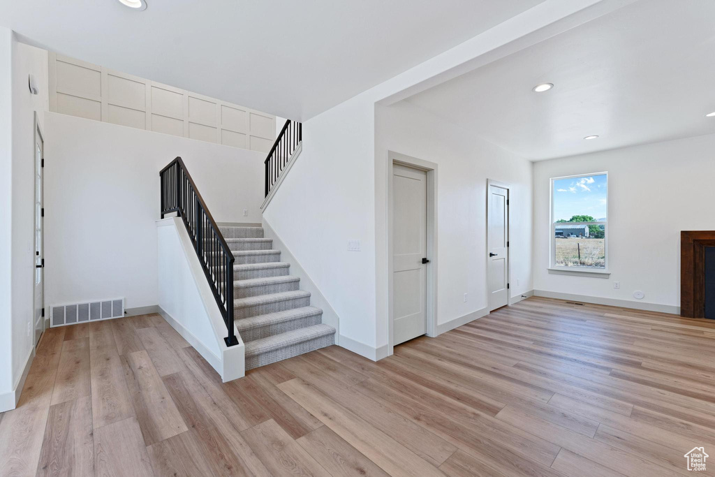 Unfurnished living room featuring stairs, light wood finished floors, recessed lighting, and baseboards