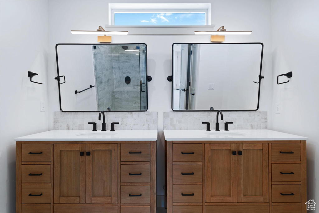 Full bath featuring backsplash, two vanities, and a shower with shower door