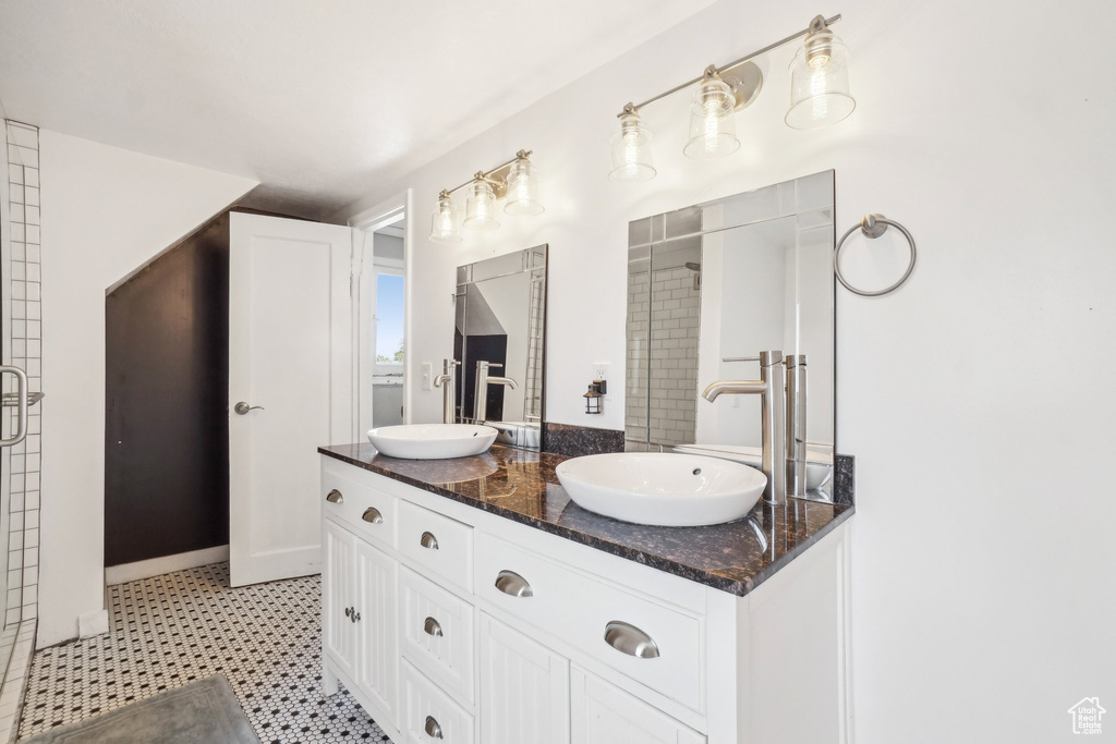 Bathroom with double vanity, tile patterned floors, and a tile shower