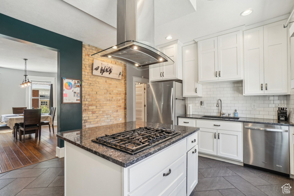 Kitchen with appliances with stainless steel finishes, island range hood, a sink, tasteful backsplash, and white cabinets