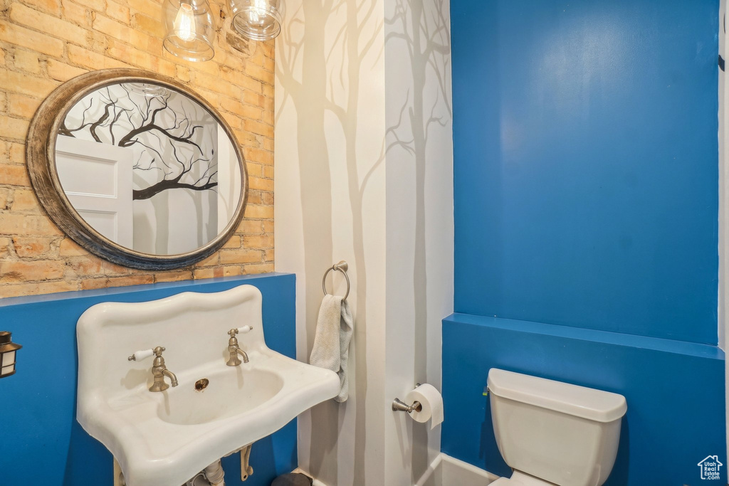 Bathroom with toilet, brick wall, and a sink