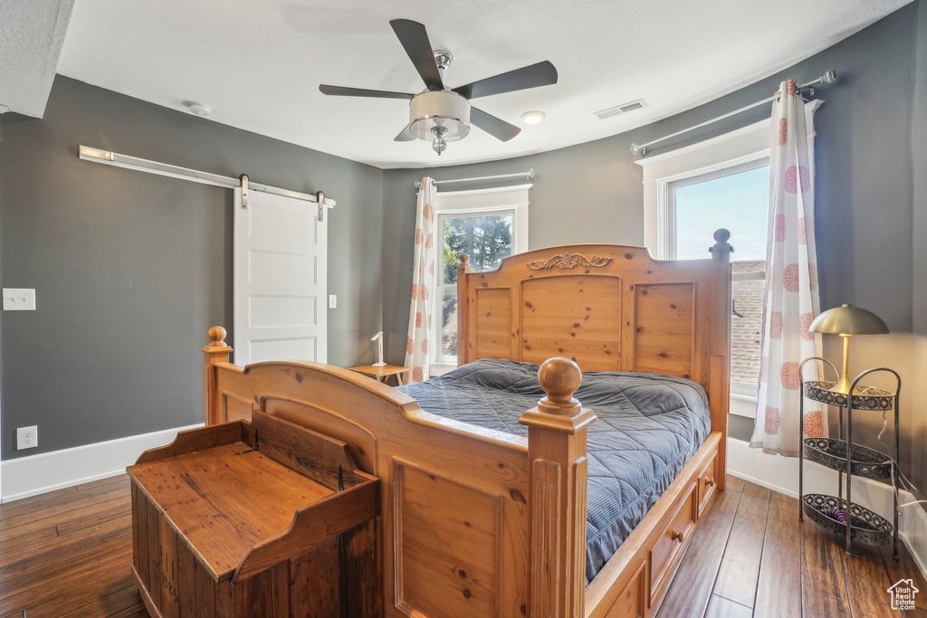 Bedroom featuring a barn door, multiple windows, baseboards, and dark wood-type flooring