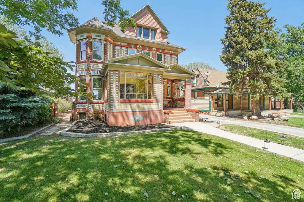 Victorian-style house with a porch, a front yard, and brick siding