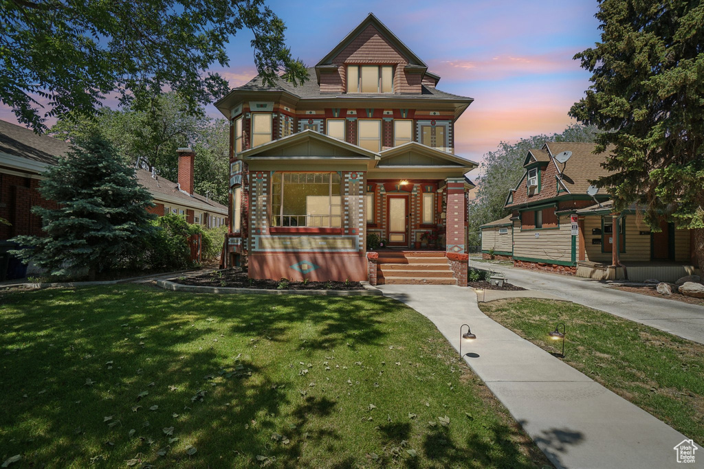 Victorian-style house featuring covered porch, a lawn, and brick siding
