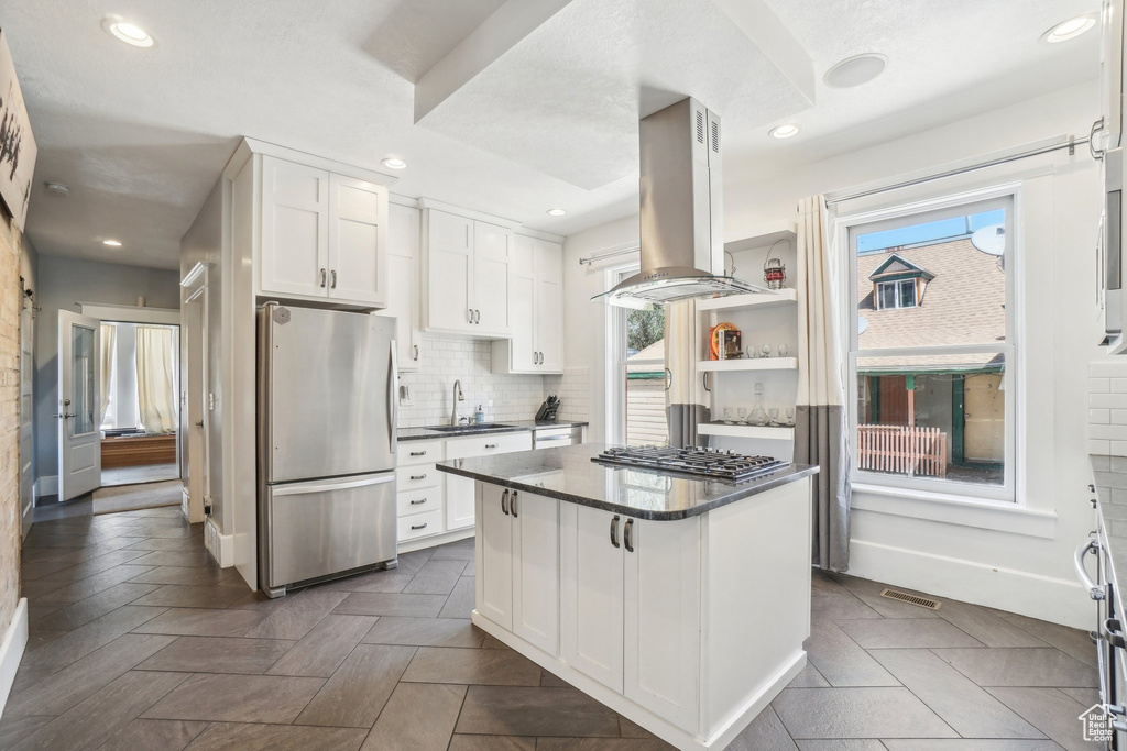 Kitchen with appliances with stainless steel finishes, island range hood, a sink, dark countertops, and white cabinets