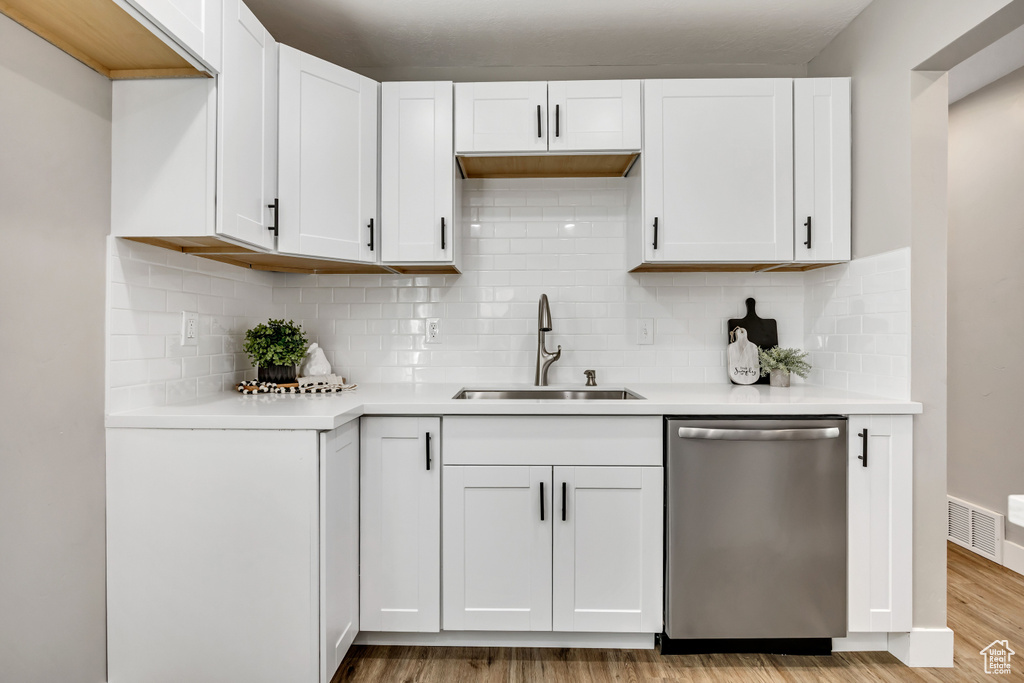 Kitchen featuring dishwasher, a sink, light wood-type flooring, light countertops, and white cabinetry
