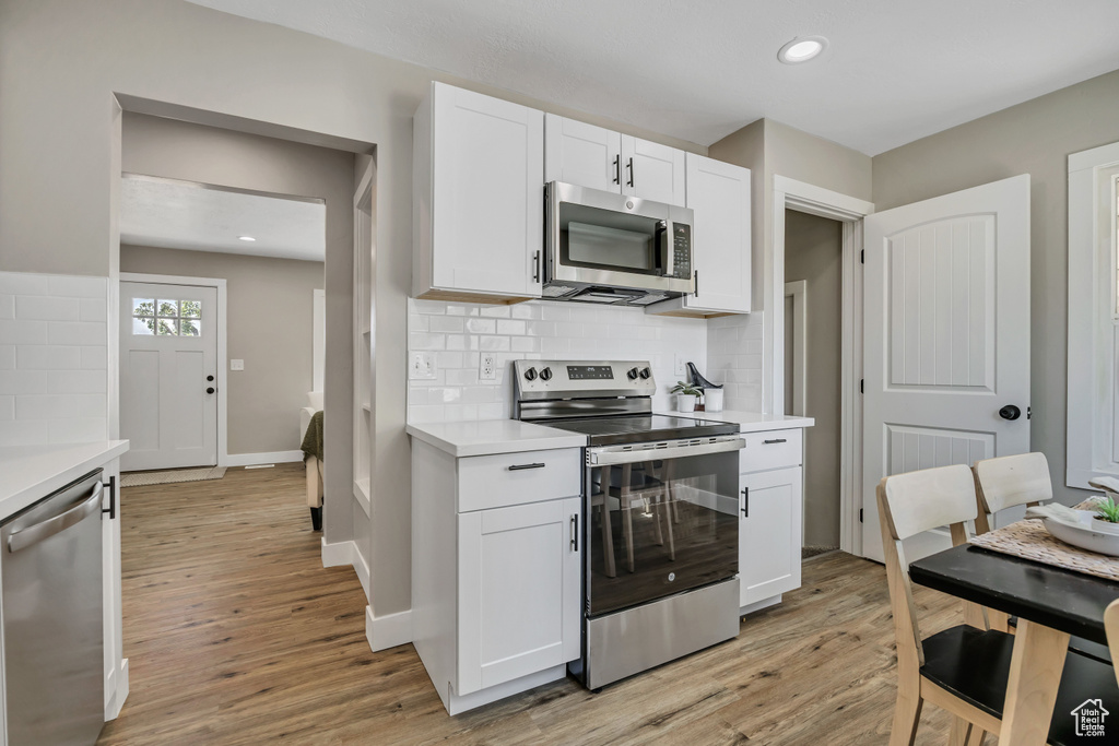 Kitchen featuring appliances with stainless steel finishes, light wood finished floors, light countertops, backsplash, and recessed lighting
