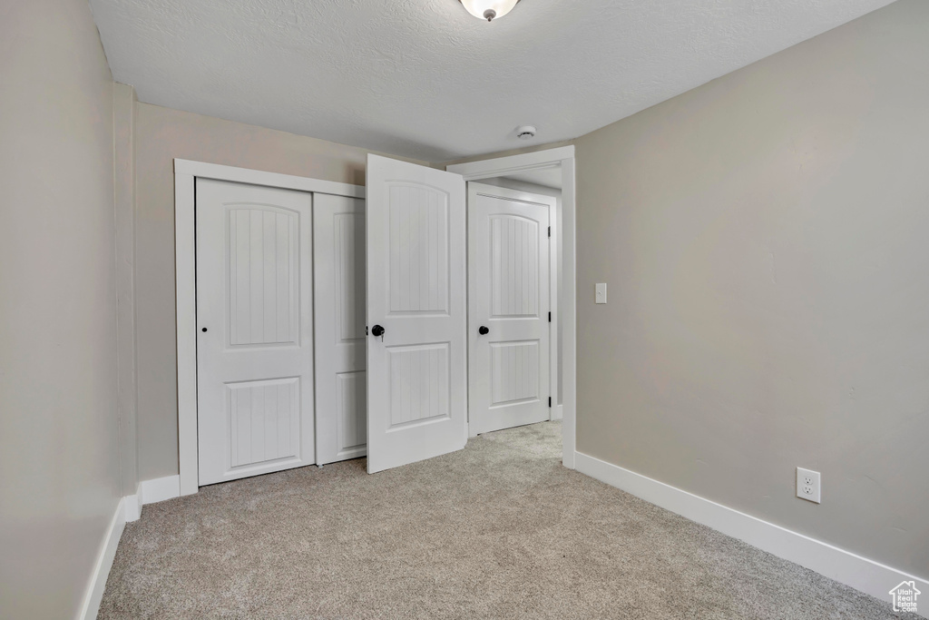Unfurnished bedroom with light carpet, baseboards, a closet, and a textured ceiling