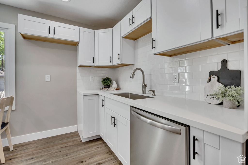 Kitchen with stainless steel dishwasher, a sink, tasteful backsplash, light wood-style flooring, and white cabinets