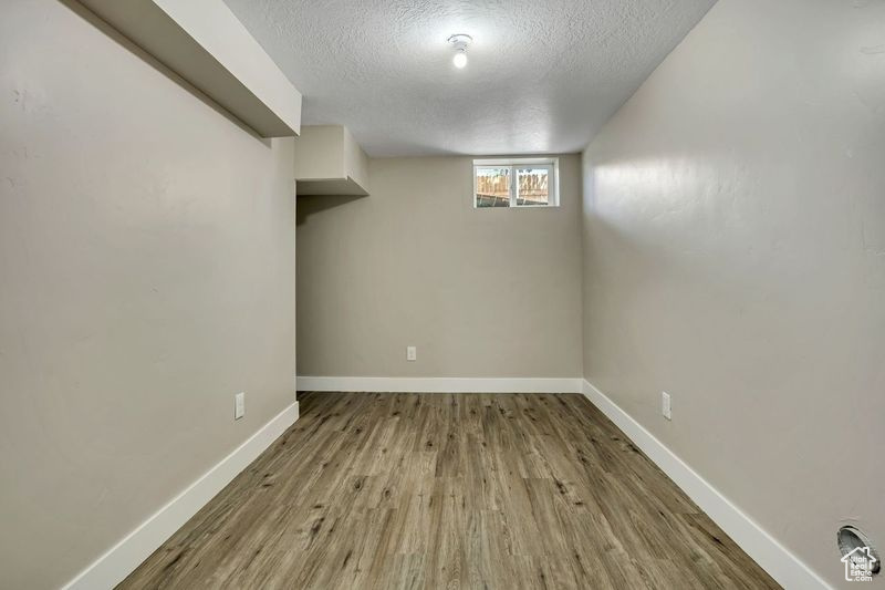 Basement with a textured ceiling, wood finished floors, and baseboards