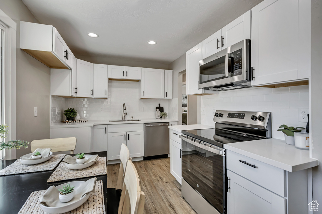 Kitchen featuring appliances with stainless steel finishes, a sink, light wood-type flooring, light countertops, and decorative backsplash