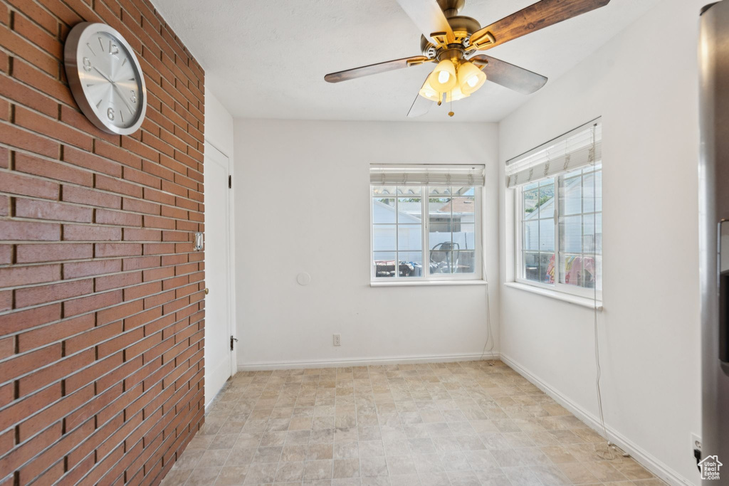 Unfurnished room featuring a ceiling fan, brick wall, and baseboards