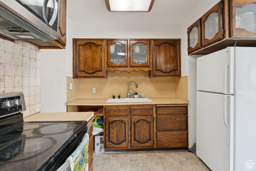Kitchen with freestanding refrigerator, black range with electric stovetop, stainless steel microwave, a sink, and light countertops