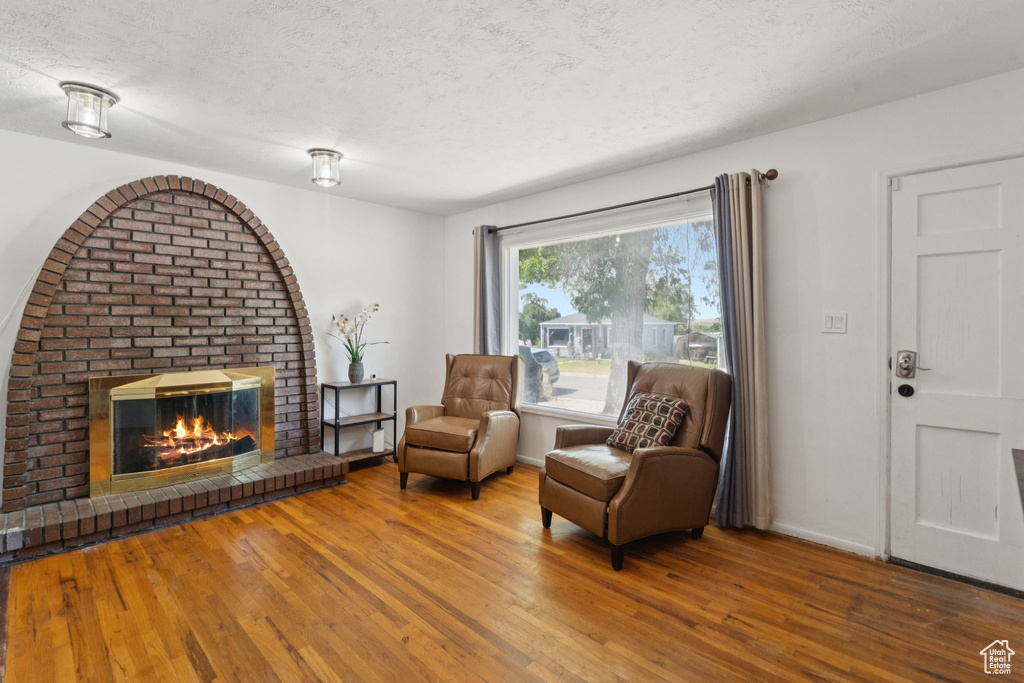 Sitting room featuring hardwood / wood-style flooring, a brick fireplace, a textured ceiling, and baseboards
