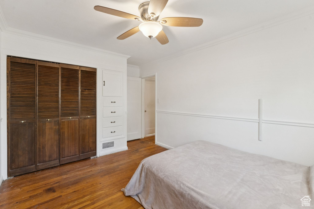 Bedroom with wood finished floors, ornamental molding, ceiling fan, and a closet