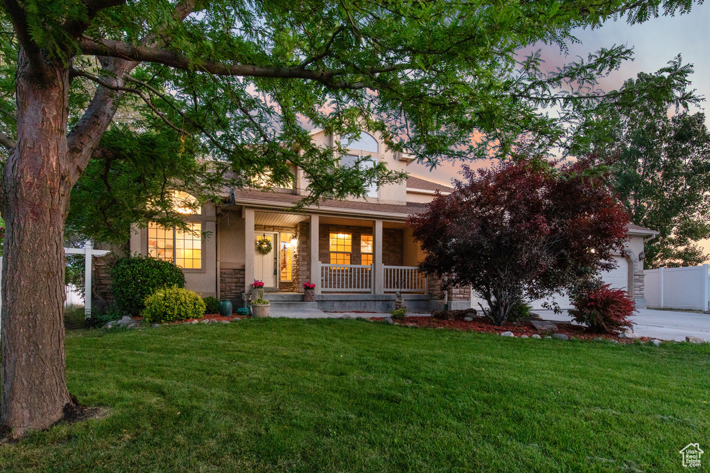 Obstructed view of property featuring a porch, a yard, stone siding, a garage, and stucco siding