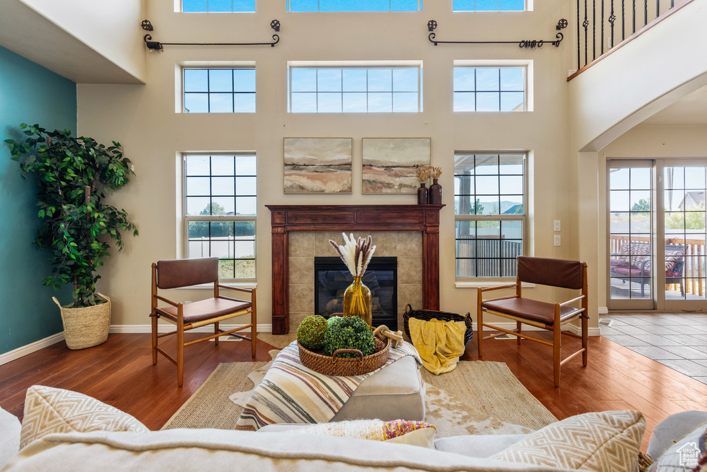 Living room featuring a high ceiling, hardwood / wood-style flooring, a tiled fireplace, baseboards, and arched walkways