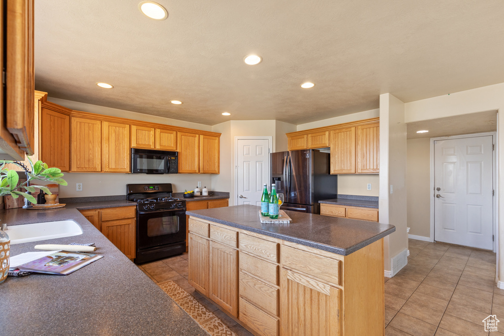 Kitchen featuring black appliances, recessed lighting, dark countertops, a center island, and light tile patterned floors