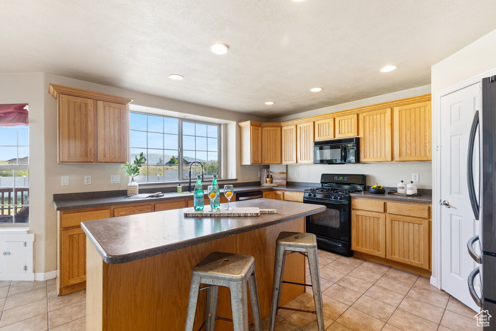 Kitchen featuring black appliances, dark countertops, light tile patterned flooring, a center island, and recessed lighting