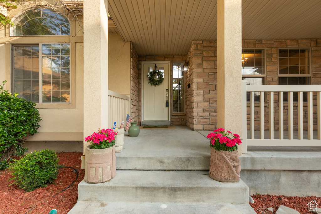 View of exterior entry with covered porch, stucco siding, and stone siding