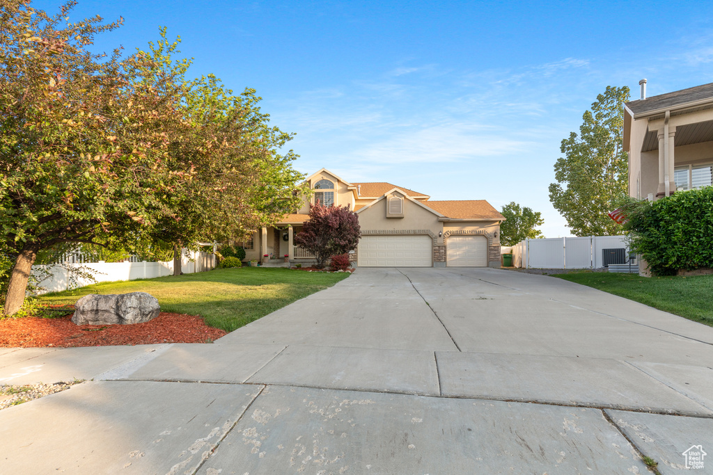 View of property hidden behind natural elements with an attached garage, driveway, stucco siding, and a gate