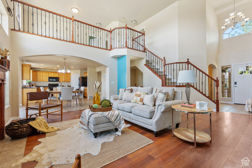 Living area with a chandelier, a towering ceiling, arched walkways, stairway, and light wood-style flooring