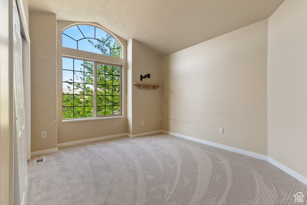 Empty room with light carpet, vaulted ceiling, and baseboards