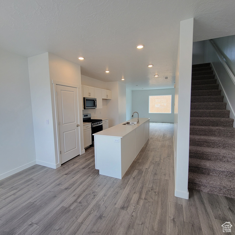 Kitchen with stainless steel microwave, black range, light wood-style floors, a sink, and recessed lighting