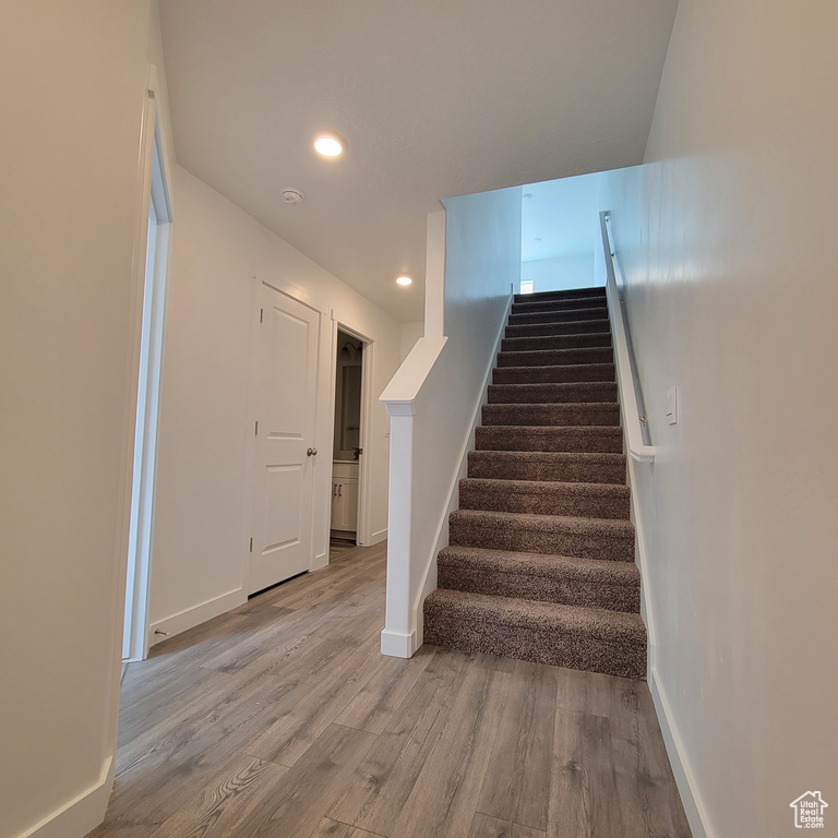 Stairs with wood finished floors, recessed lighting, and baseboards